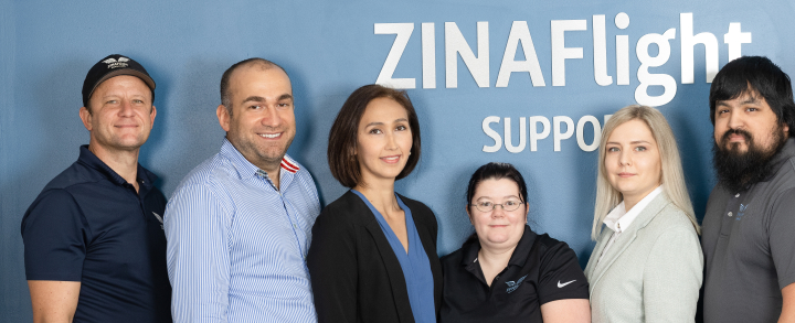 Six team members standing in front of a wall with "ZINAFlight Support" written on it.